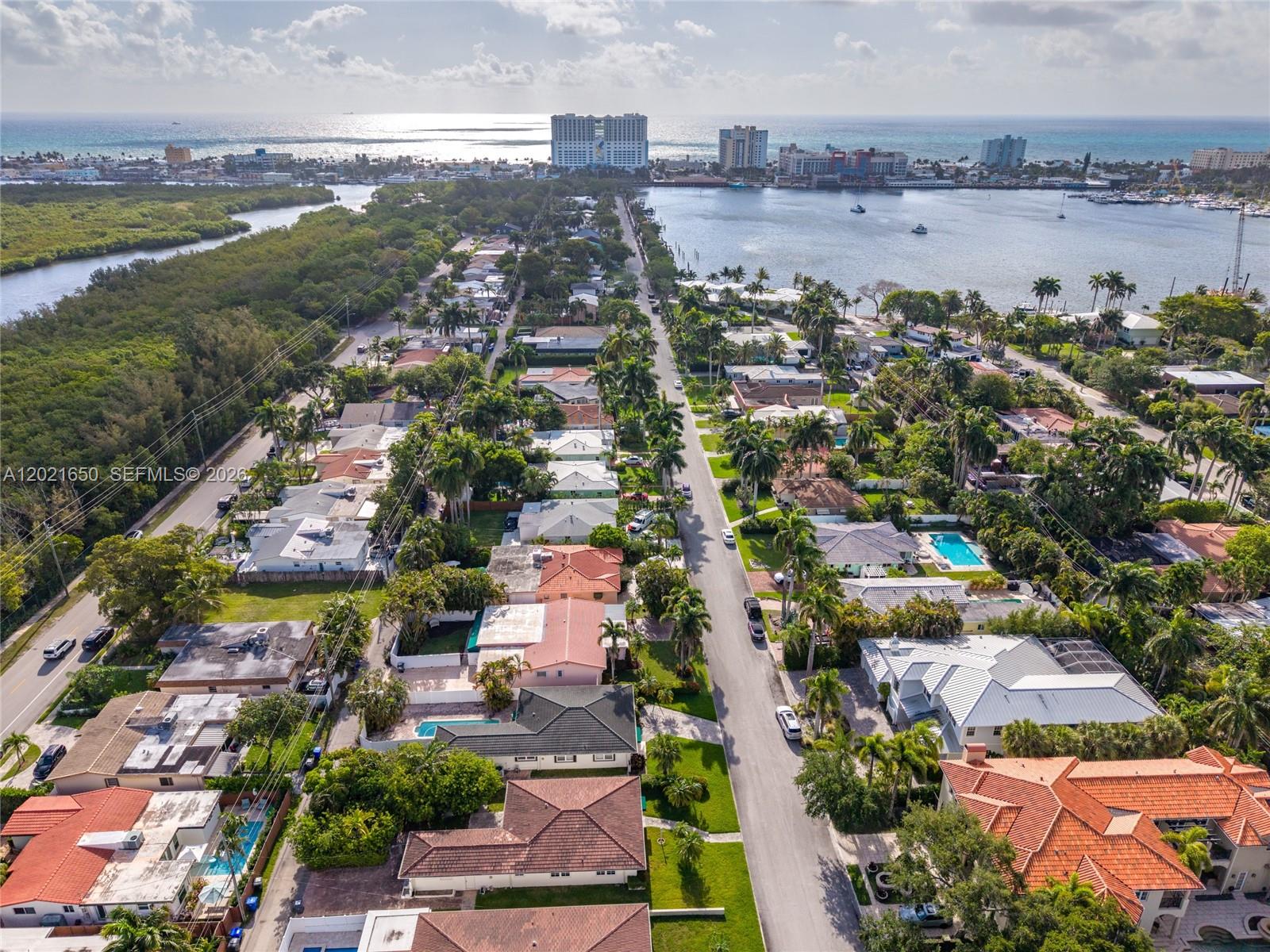 An aerial view shows a residential street with houses, palm trees, and a nearby bay — 947 Lincoln St, Hollywood FL 33019, HOLLYWOOD, FL