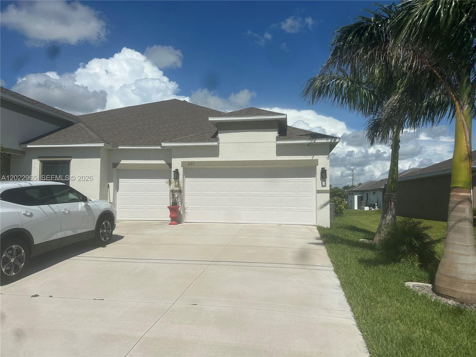 A white house with a three-car garage and a concrete driveway under a blue sky — 225 SW 31ST PL, Cape Coral FL 33991, CAPE CORAL, FL