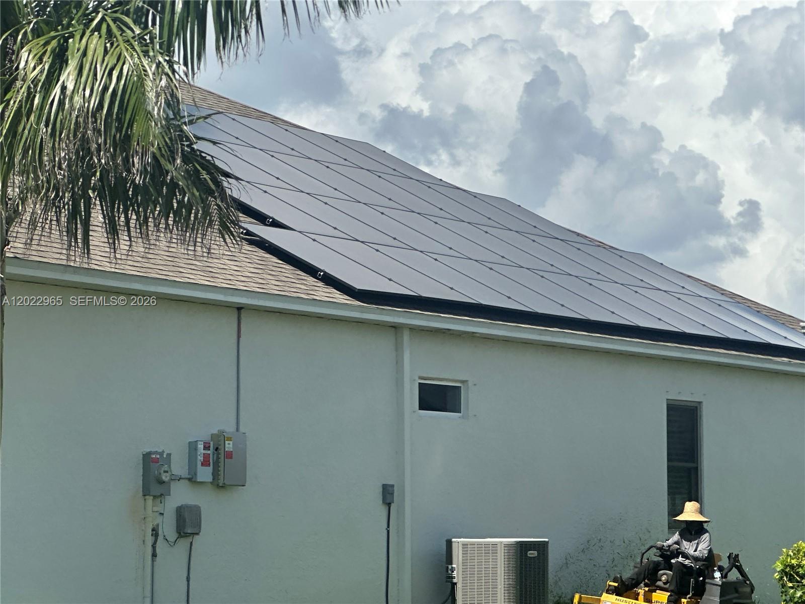 A house exterior features a large roof-mounted solar panel array and a person on a mower — 225 SW 31ST PL, Cape Coral FL 33991, CAPE CORAL, FL