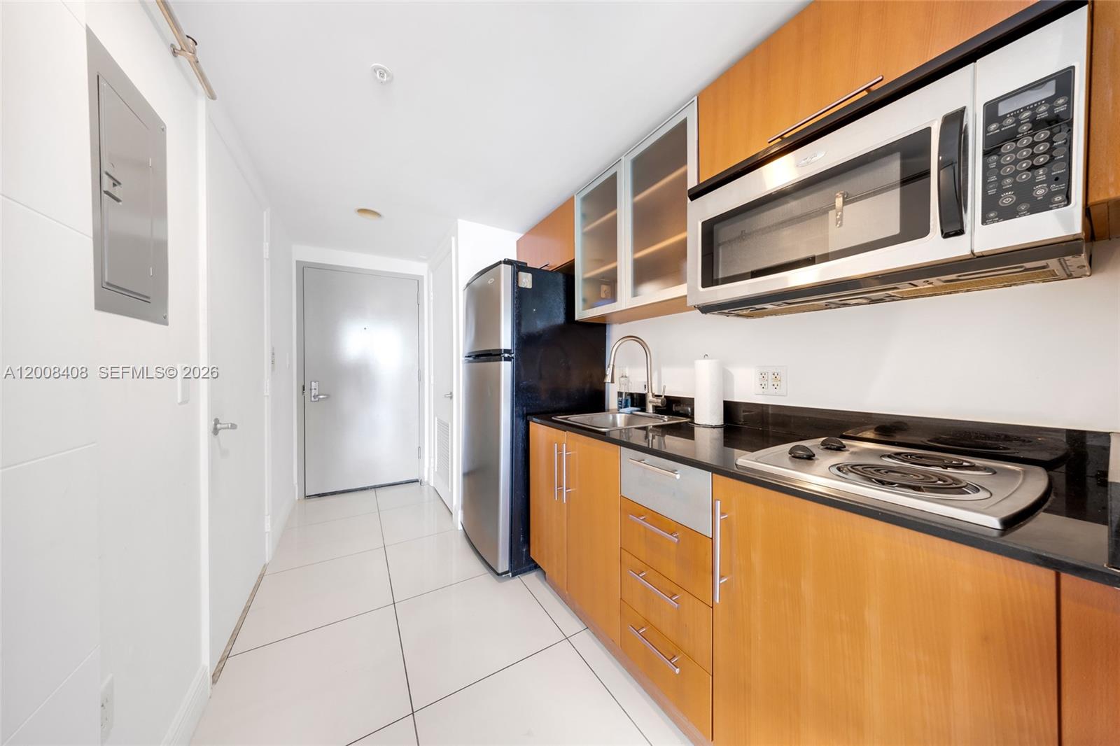 A galley kitchen features wood cabinets, black countertops, stainless steel appliances, and white tile flooring — 1750 N Bayshore Dr # 3308, Miami FL 33132, MIAMI, FL