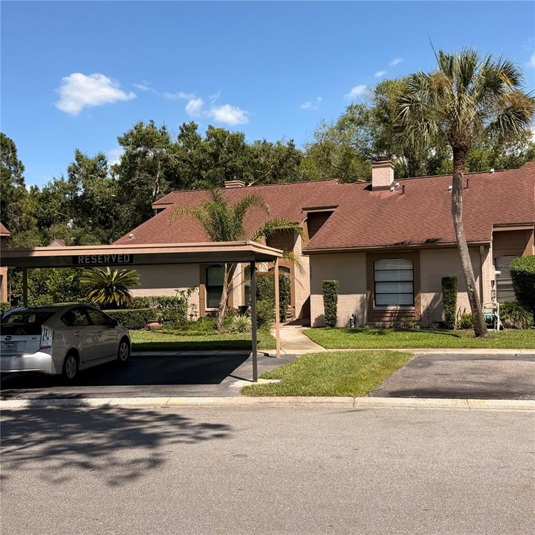 A tan, single-story residential building features a brown shingled roof and a reserved carport — 3409 HILL MOOR DRIVE, PALM HARBOR, FL