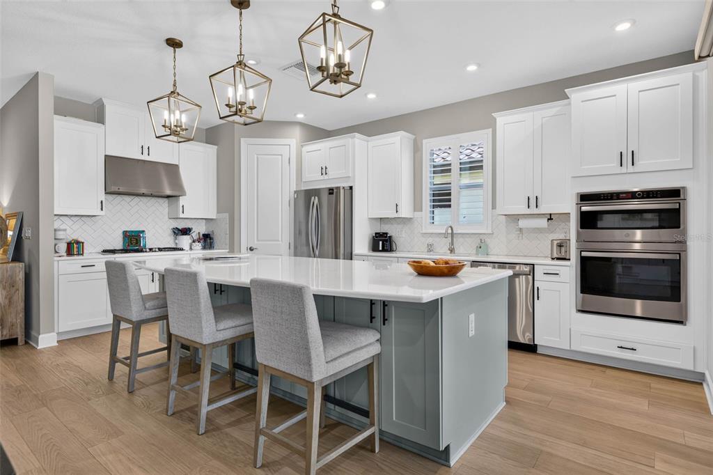 A modern kitchen features white cabinets, a gray island with bar stools, and stainless appliances — 11108 CALLUNA DRIVE, ODESSA, FL