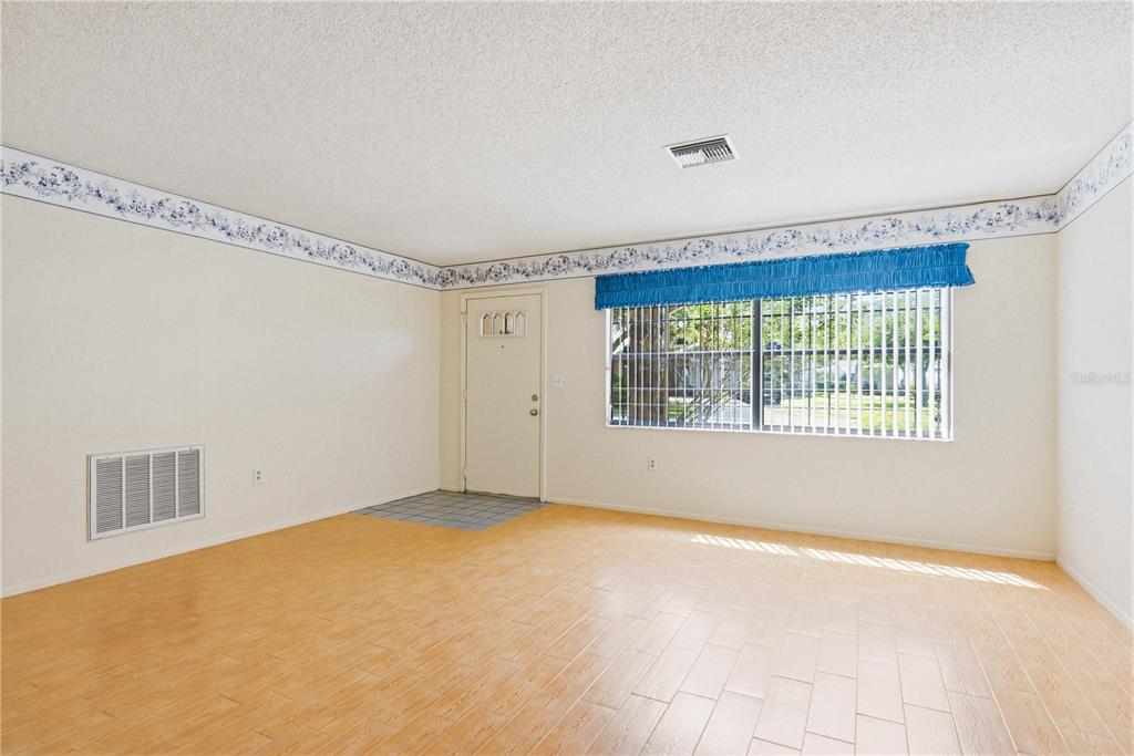An empty room with light wood-look tile flooring, a white front door, and floral wallpaper border — 7832 MCPHERSON DRIVE, NEW PORT RICHEY, FL