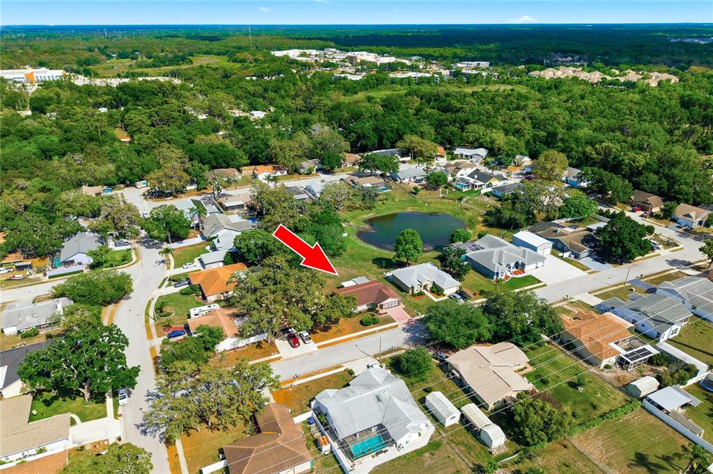 An aerial view shows a single-story house with a red roof near a small pond — 7832 MCPHERSON DRIVE, NEW PORT RICHEY, FL