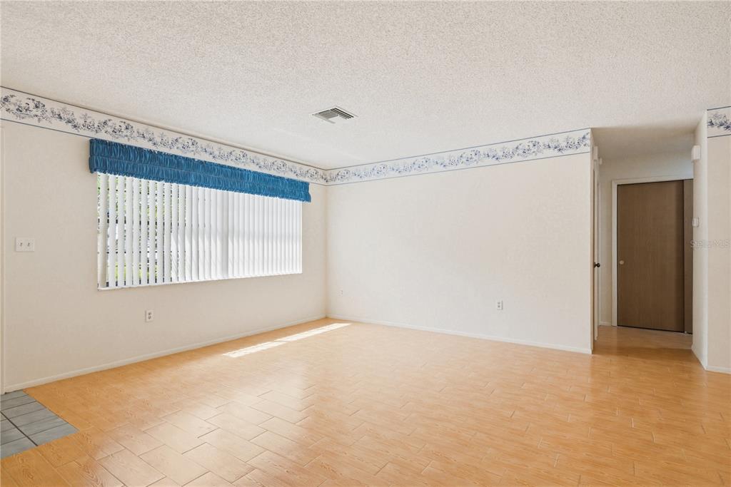 An empty room features light wood-look tile flooring, beige walls with blue floral wallpaper borders — 7832 MCPHERSON DRIVE, NEW PORT RICHEY, FL