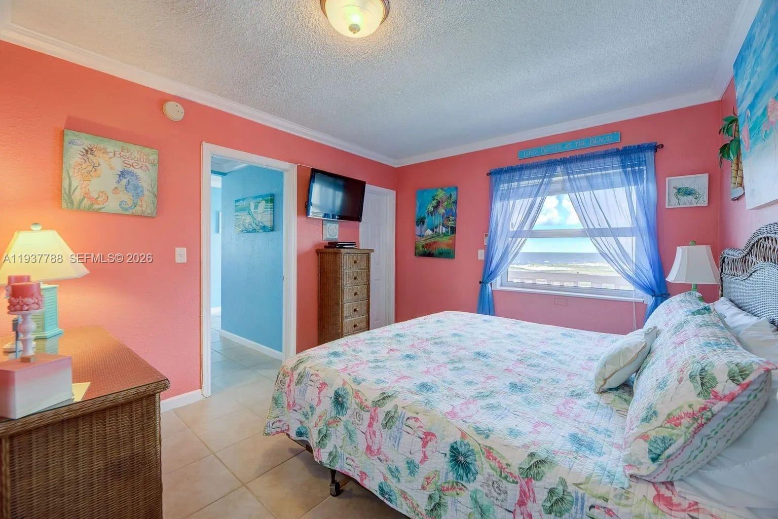 A bedroom features coral walls, a floral bedspread, a wicker dresser, and a beach view — 3401 NE 10th St # 12, Pompano Beach FL 33062, POMPANO BEACH, FL