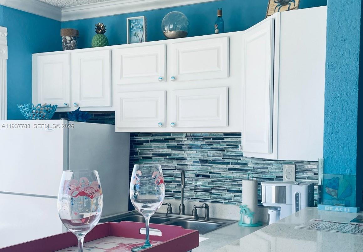 A kitchen features white cabinets, a blue mosaic tile backsplash, and a sink area — 3401 NE 10th St # 12, Pompano Beach FL 33062, POMPANO BEACH, FL