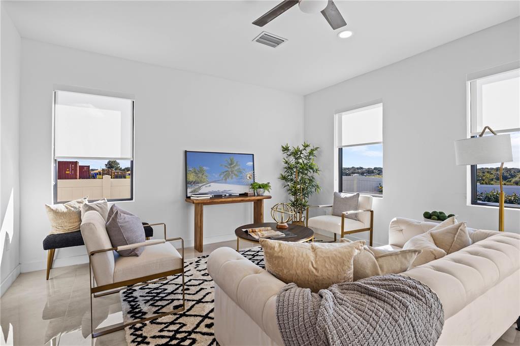 A bright living room features a tufted sofa, two accent chairs, and a television console — 6414 QUARTET STREET, MASCOTTE, FL
