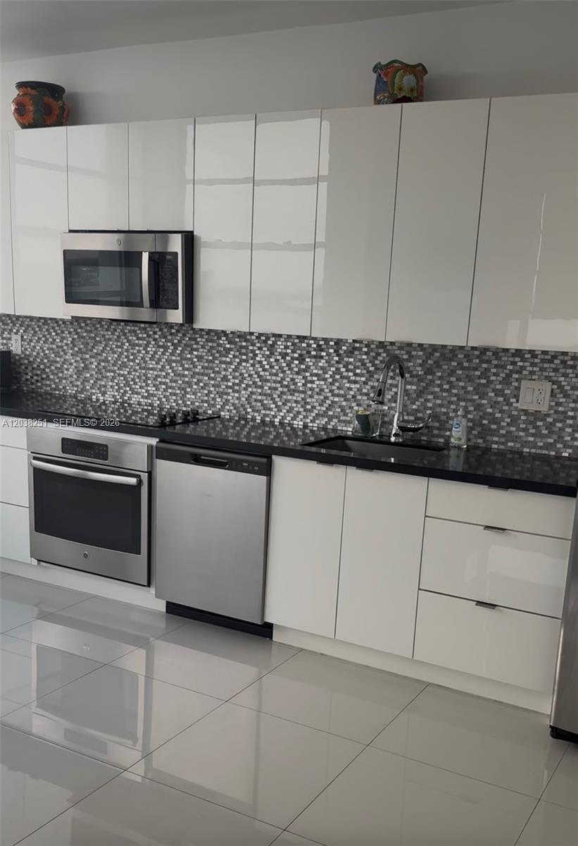 A modern kitchen features white high-gloss cabinets, stainless steel appliances, and a mosaic tile backsplash — 11930 N Bayshore Dr # 8, North Miami FL 33181, NORTH MIAMI, FL