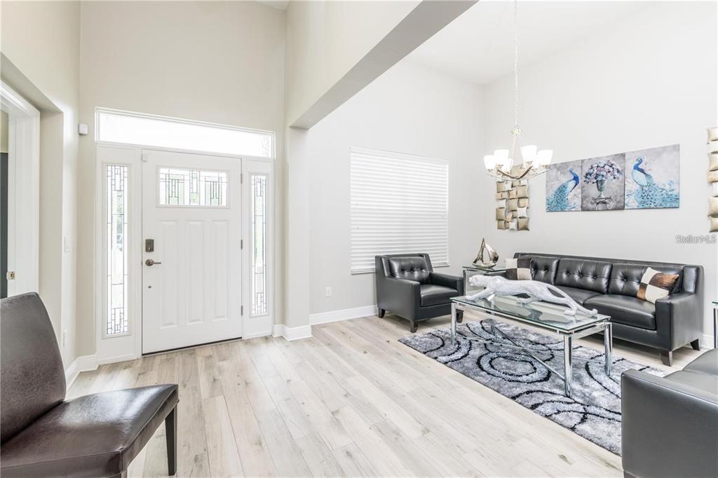 A bright living room features light wood floors, a white front door, and black leather furniture — 5816 LITTLE RIVER DRIVE, TAMPA, FL