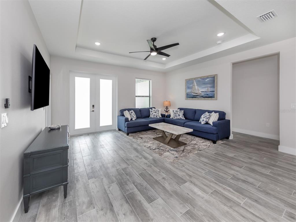 A living room features a blue sectional sofa, a coffee table, and a tray ceiling — 17566 DE MIRANDA AVENUE, NORTH PORT, FL
