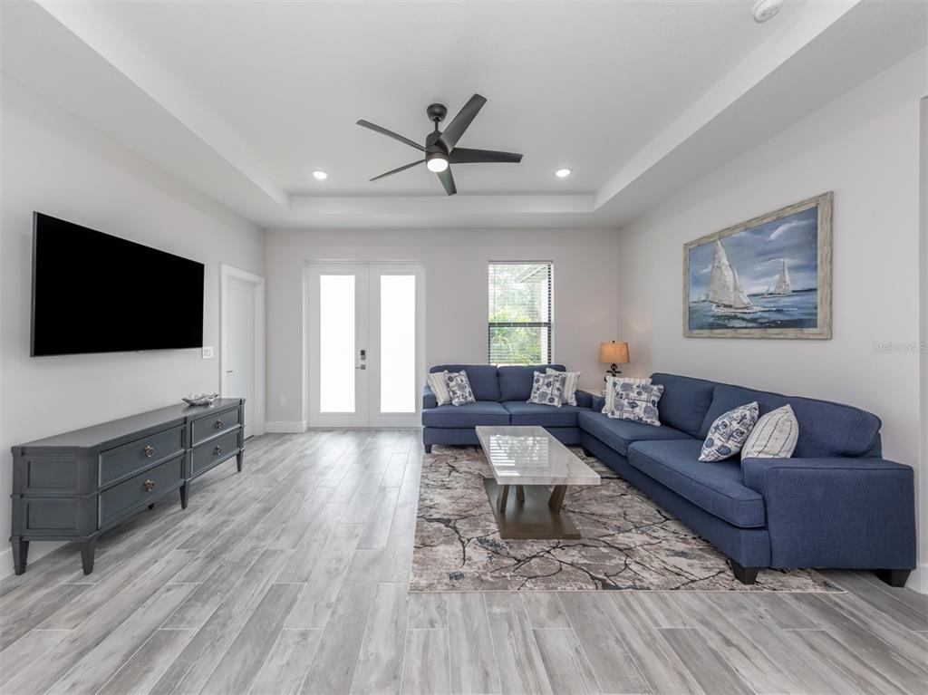 A living room features a blue sectional sofa, a television, and wood-look tile flooring — 17566 DE MIRANDA AVENUE, NORTH PORT, FL