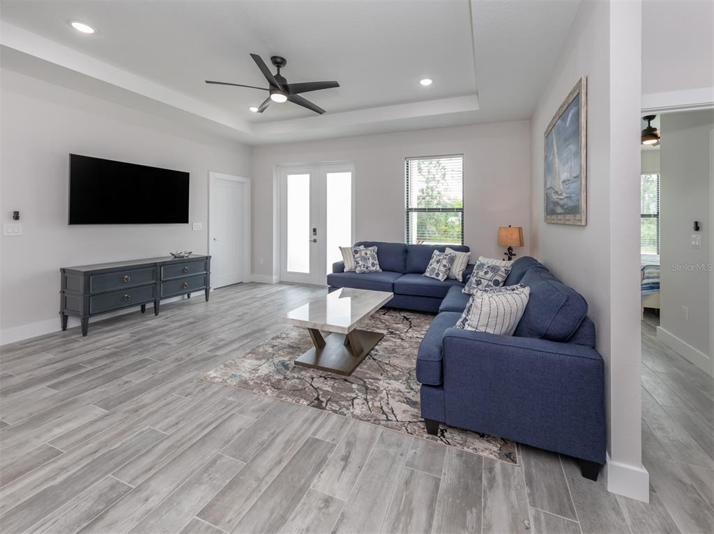 A living room with a blue sectional sofa, gray wood-look tile floors, and a television — 17566 DE MIRANDA AVENUE, NORTH PORT, FL
