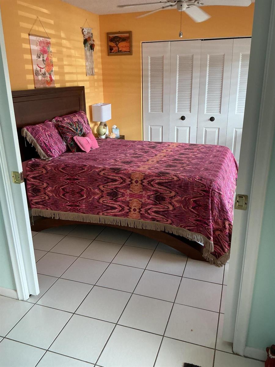 A bedroom with orange walls, a dark wood bed frame, and a patterned pink bedspread — 1580 NW 18th Avenue # B, Delray Beach FL 33445, DELRAY BEACH, FL