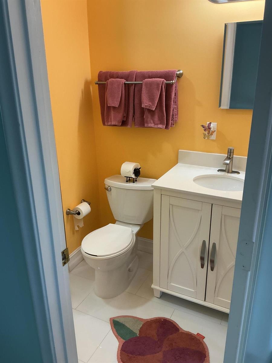 A small bathroom features orange walls, a white vanity, a toilet, and mauve towels — 1580 NW 18th Avenue # B, Delray Beach FL 33445, DELRAY BEACH, FL