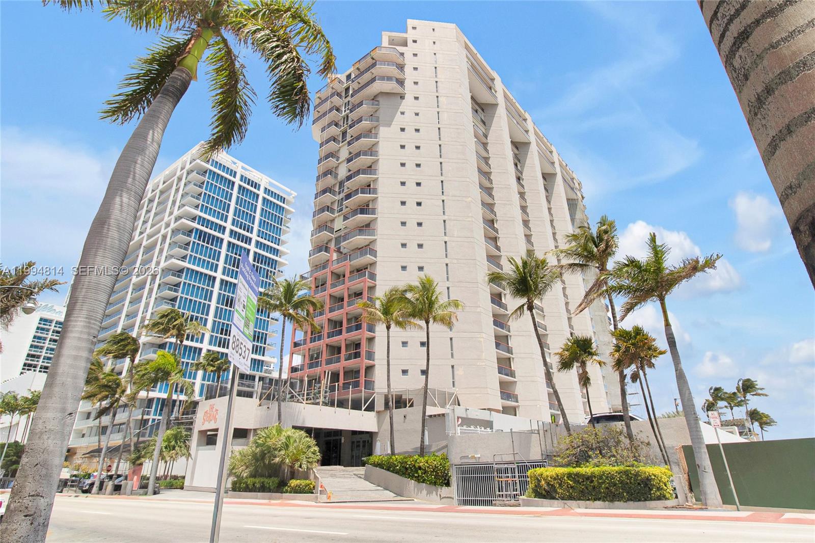 A tall, light-colored residential building stands next to a modern glass skyscraper under a blue sky — 6767 Collins Ave # 504, Miami Beach FL 33141, MIAMI BEACH, FL
