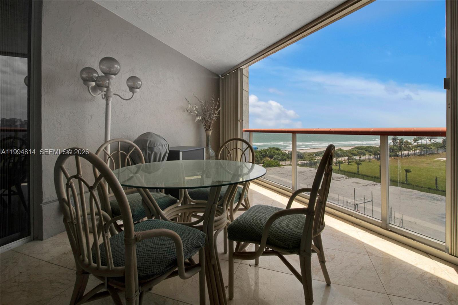 A balcony features a glass-topped table with four chairs and an ocean view — 6767 Collins Ave # 504, Miami Beach FL 33141, MIAMI BEACH, FL