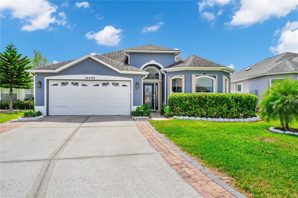 A blue single-story house with a two-car garage, arched entryway, and landscaped front yard — 10209 ANDOVER POINT CIRCLE, ORLANDO, FL