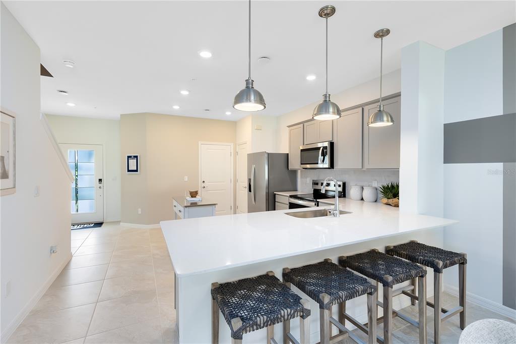 A modern kitchen features a white quartz island with bar stools and stainless steel appliances — 3246 PONDSIDE WAY, SANFORD, FL