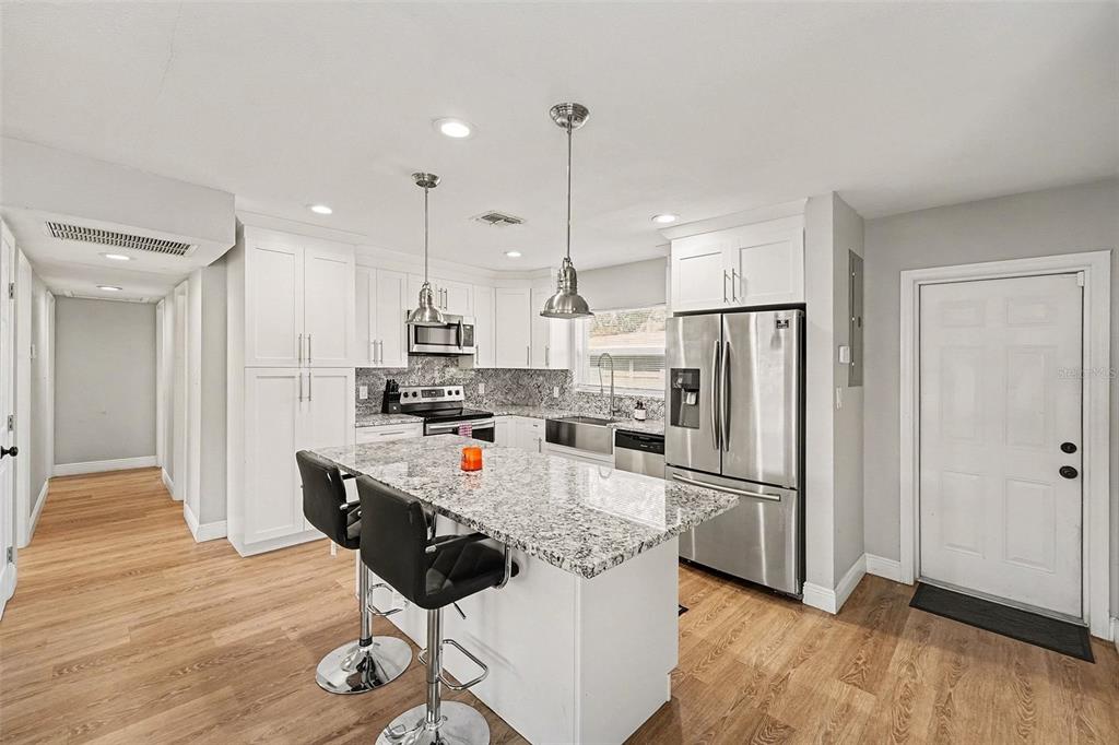 A kitchen with white cabinets, granite countertops, a center island with stools, and stainless appliances — 6504 N 21ST STREET, TAMPA, FL