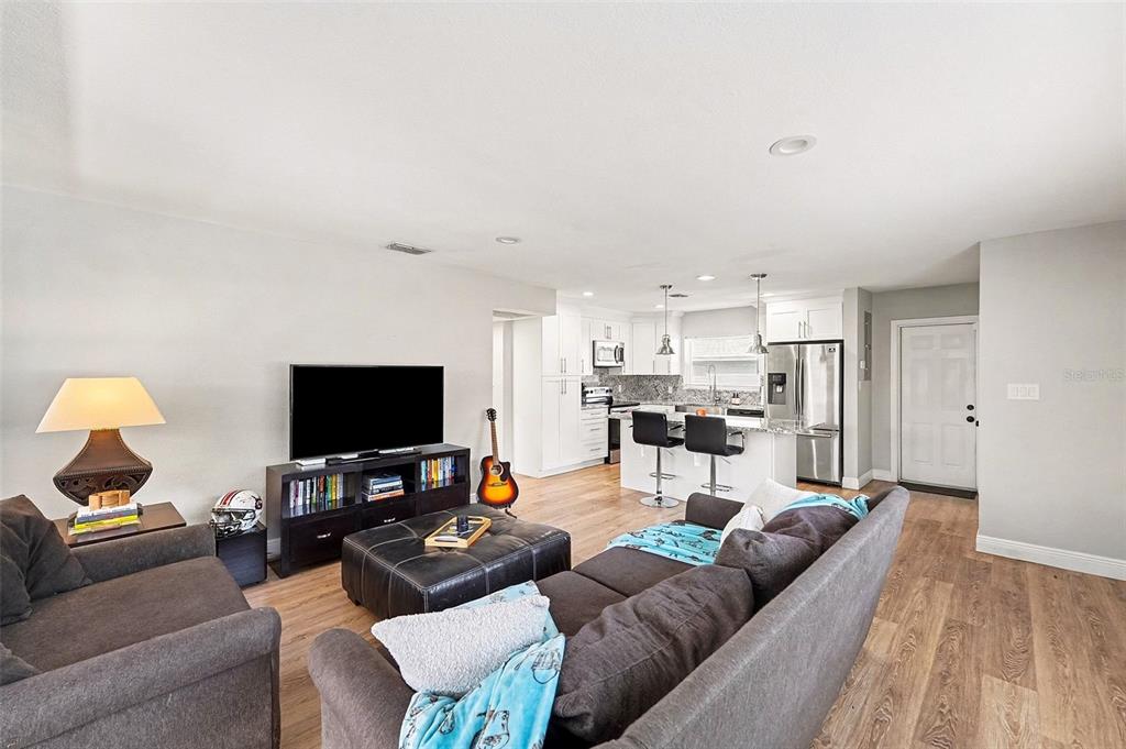 A living room with wood-look flooring opens to a kitchen with white cabinets and stainless appliances — 6504 N 21ST STREET, TAMPA, FL