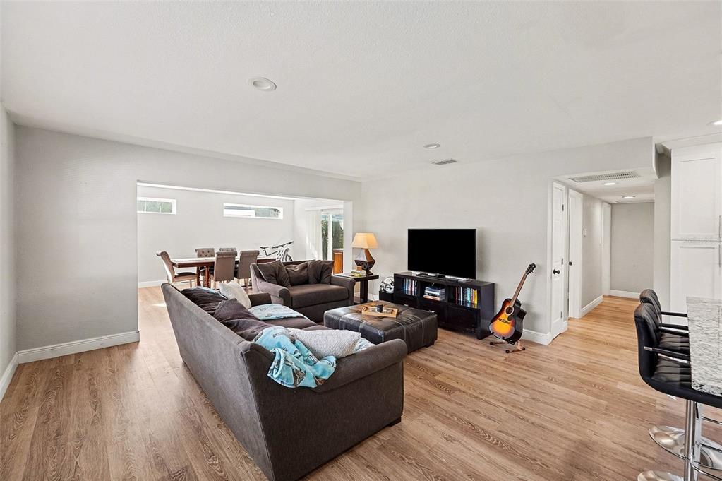 A living room with wood-look flooring, a gray sofa, and an open dining area — 6504 N 21ST STREET, TAMPA, FL