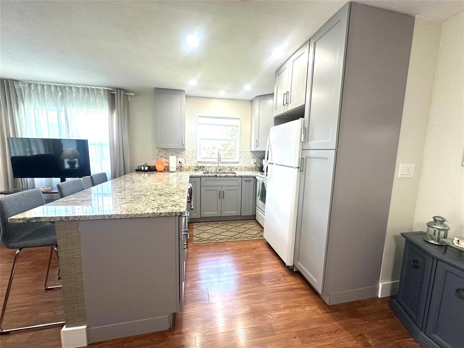 A kitchen features gray cabinets, granite countertops, a white refrigerator, and wood-look flooring — 528 Tilford X # 528, Deerfield Beach FL 33442, DEERFIELD BEACH, FL