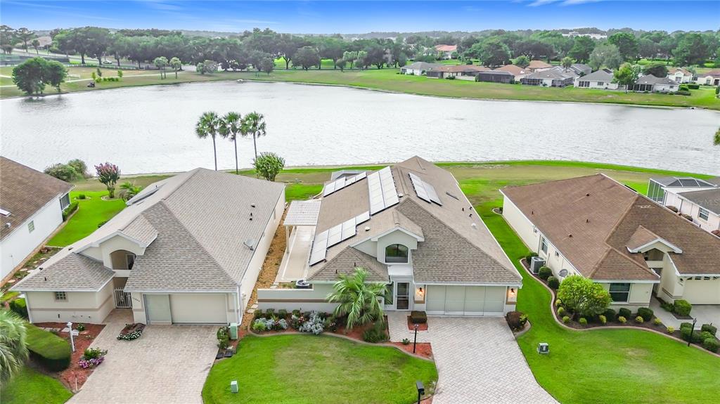 An aerial view shows three suburban houses with tiled roofs situated along a large lake — 11363 SE 177TH LANE, SUMMERFIELD, FL