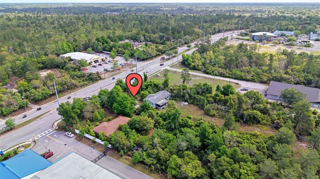 An aerial view shows a house surrounded by trees near a road and commercial buildings — 3021 HOWLAND BOULEVARD, DELTONA, FL