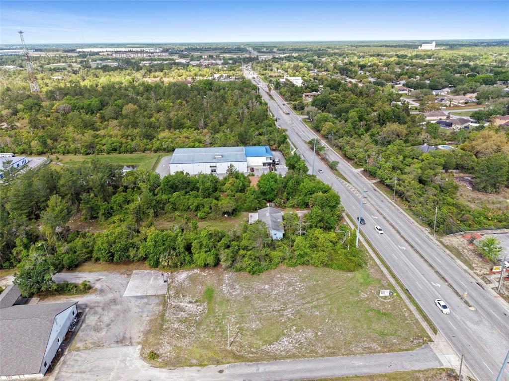 An aerial view shows a vacant lot, a small house, and a warehouse along a road — 3021 HOWLAND BOULEVARD, DELTONA, FL