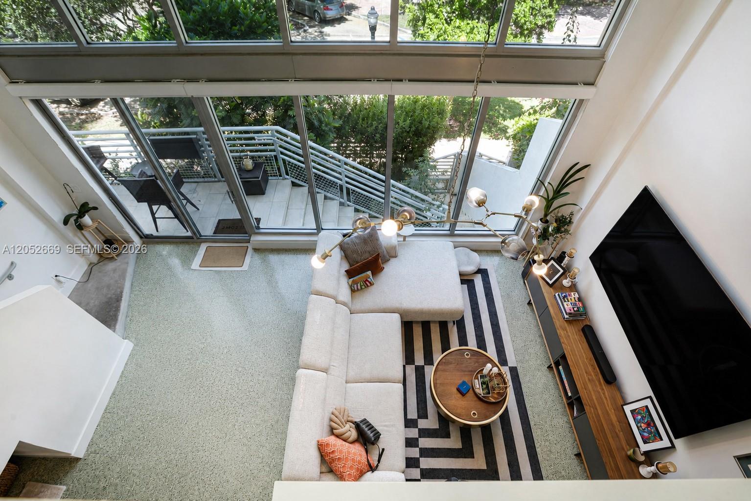A high-angle view of a modern living room with a sectional sofa and floor-to-ceiling windows — 245 Michigan Ave # 5, Miami Beach FL 33139, MIAMI BEACH, FL