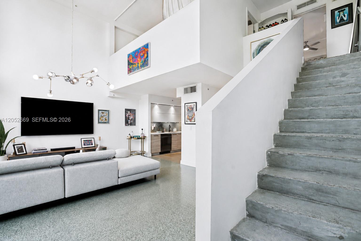 A living room with a gray sectional sofa, concrete stairs, and a lofted area — 245 Michigan Ave # 5, Miami Beach FL 33139, MIAMI BEACH, FL