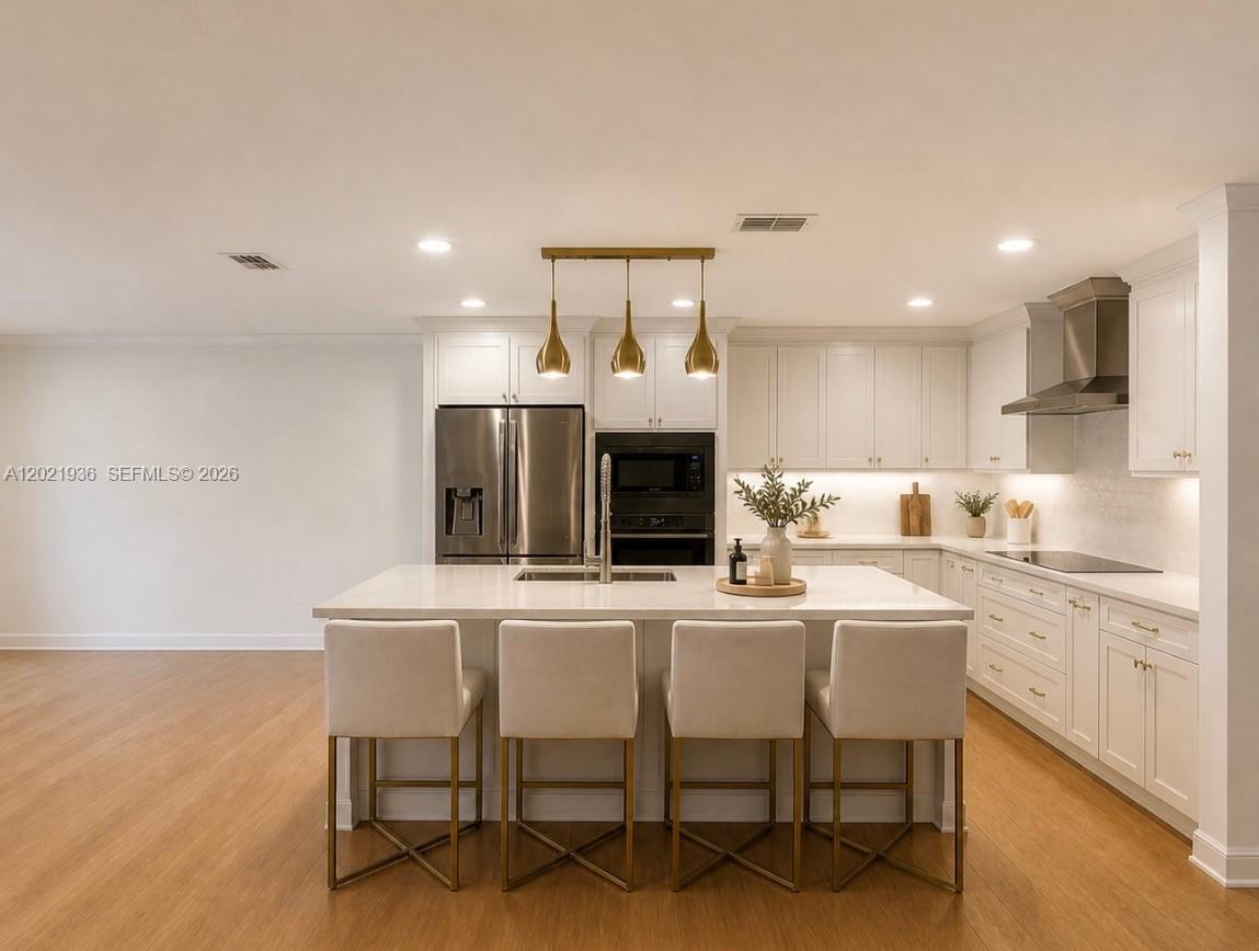 A modern kitchen features white cabinetry, a central island with bar seating, and gold lighting — 16342 SW 45th Ter, Miami FL 33185, MIAMI, FL