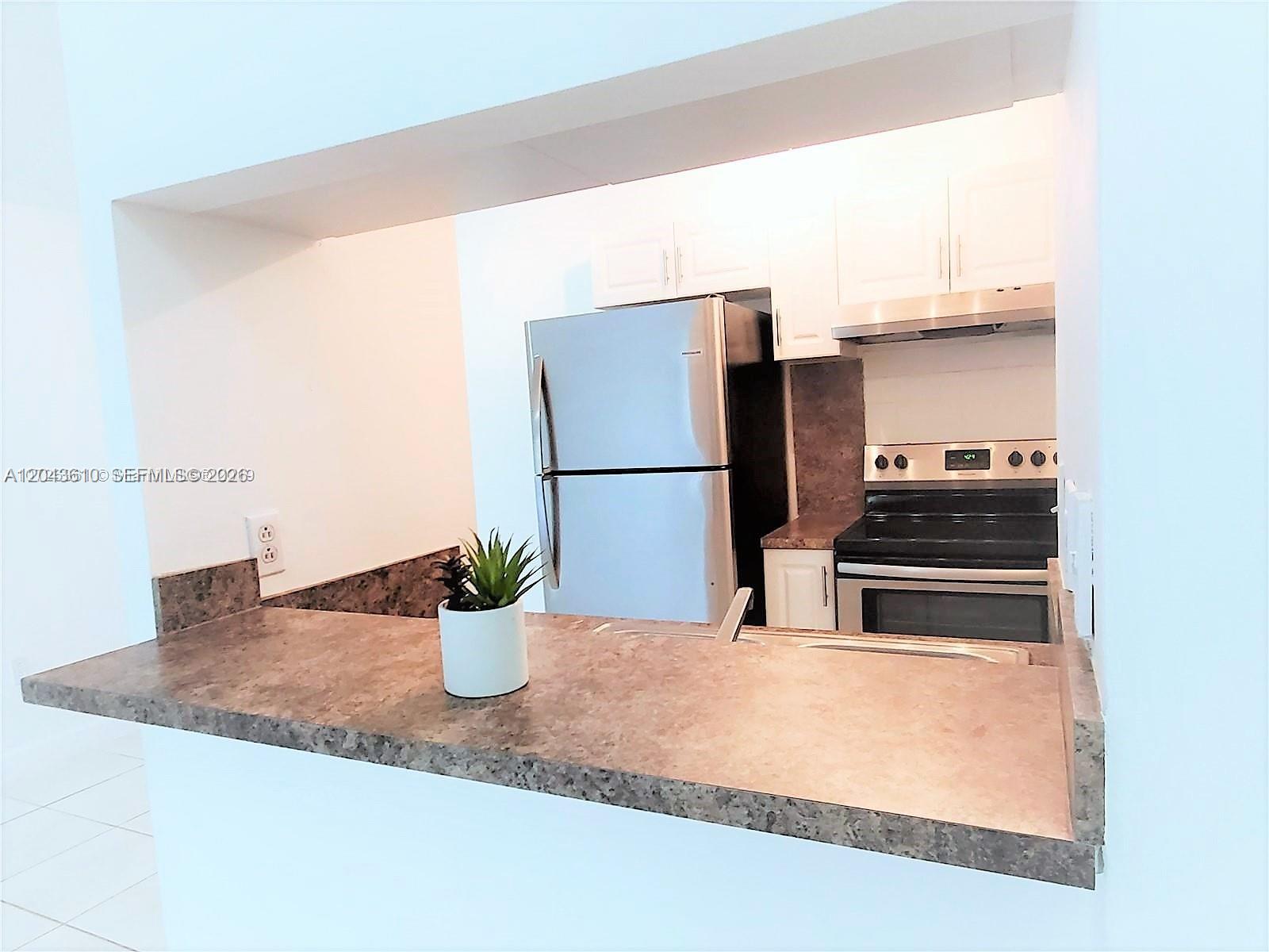 A kitchen features a breakfast bar, stainless steel refrigerator, and white cabinetry — 15659 SW 73rd Cir Ter # 4, Miami FL 33193, MIAMI, FL