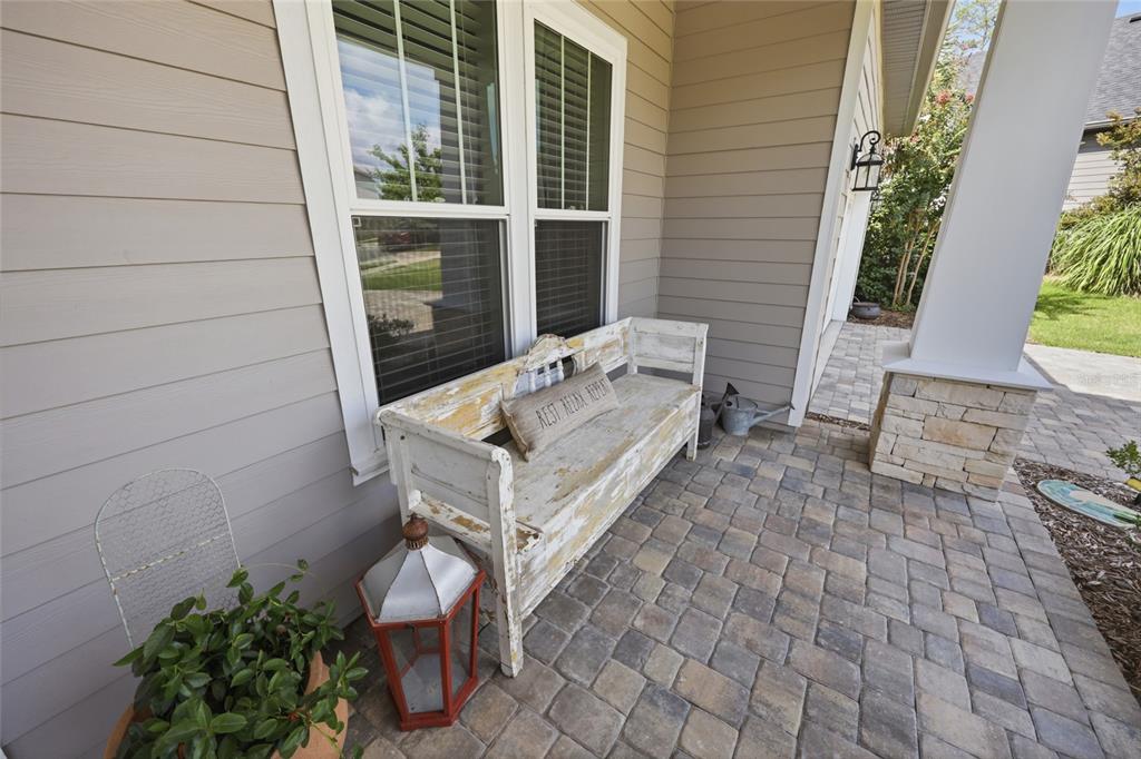 A weathered white wooden bench sits on a paved porch next to a house window — 13417 NW 10TH LANE, NEWBERRY, FL