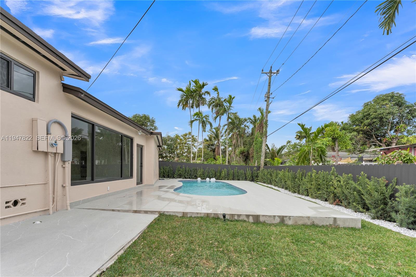A backyard features a swimming pool, a concrete patio, and a tall privacy fence — 141 NE 122nd St, North Miami FL 33161, NORTH MIAMI, FL