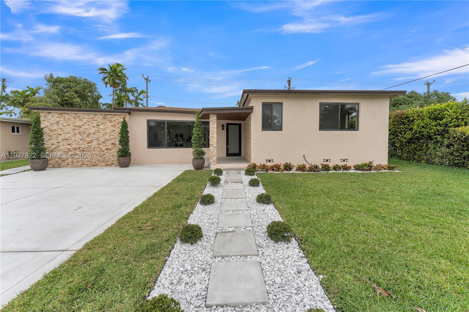 The exterior of a single-story house features a stone facade, a concrete driveway, and a walkway — 141 NE 122nd St, North Miami FL 33161, NORTH MIAMI, FL