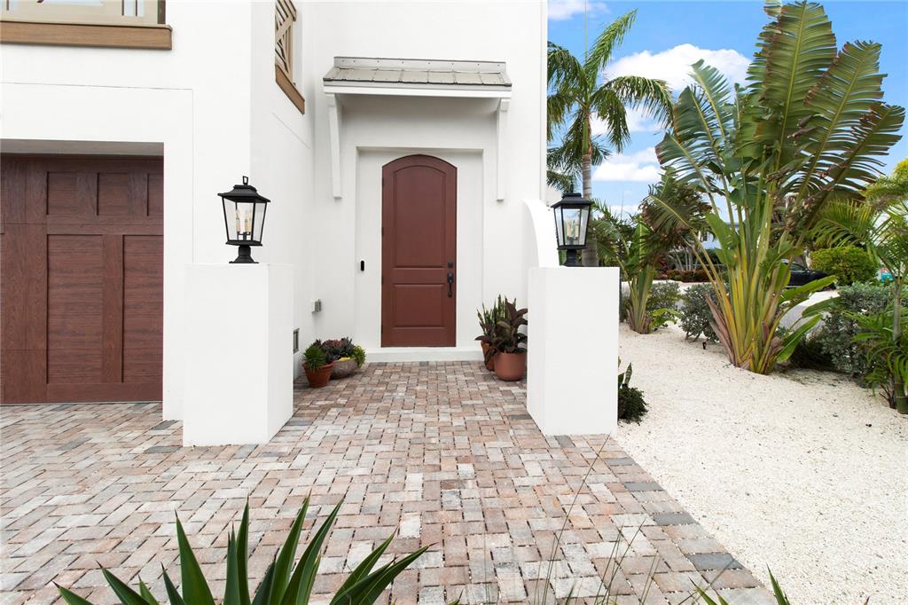 A white house exterior features a brown arched front door, brick pavers, and landscaping — 416 ALAMANDA ROAD, ANNA MARIA, FL