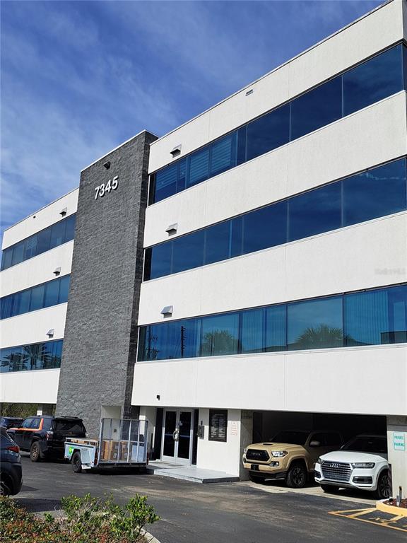 A four-story office building with a gray stone facade and a ground-level parking area — 7345 W SAND LAKE ROAD UNIT 316, ORLANDO, FL