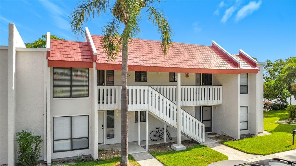 A two-story apartment building features a red shingled roof, white stucco walls, and stairs — 1801 GULF DRIVE N UNIT 248, BRADENTON BEACH, FL
