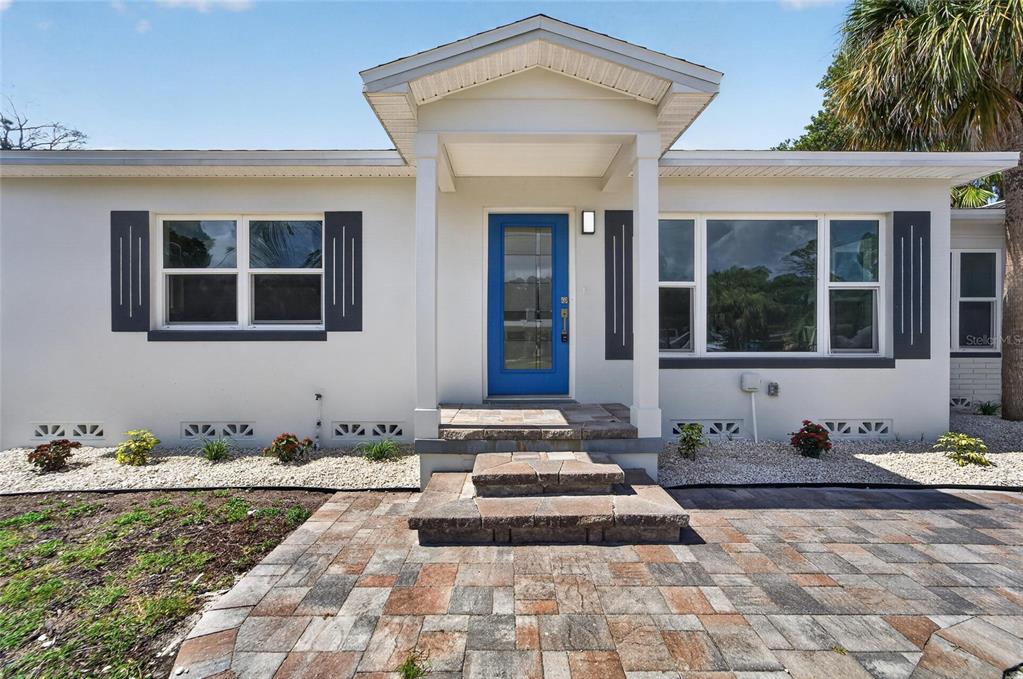 A single-story house with white stucco walls, a blue front door, and stone steps — 4810 DEL RIO WAY S, GULFPORT, FL
