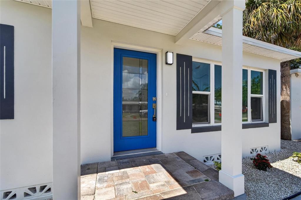 A bright blue front door with a glass panel sits under a covered porch entrance — 4810 DEL RIO WAY S, GULFPORT, FL