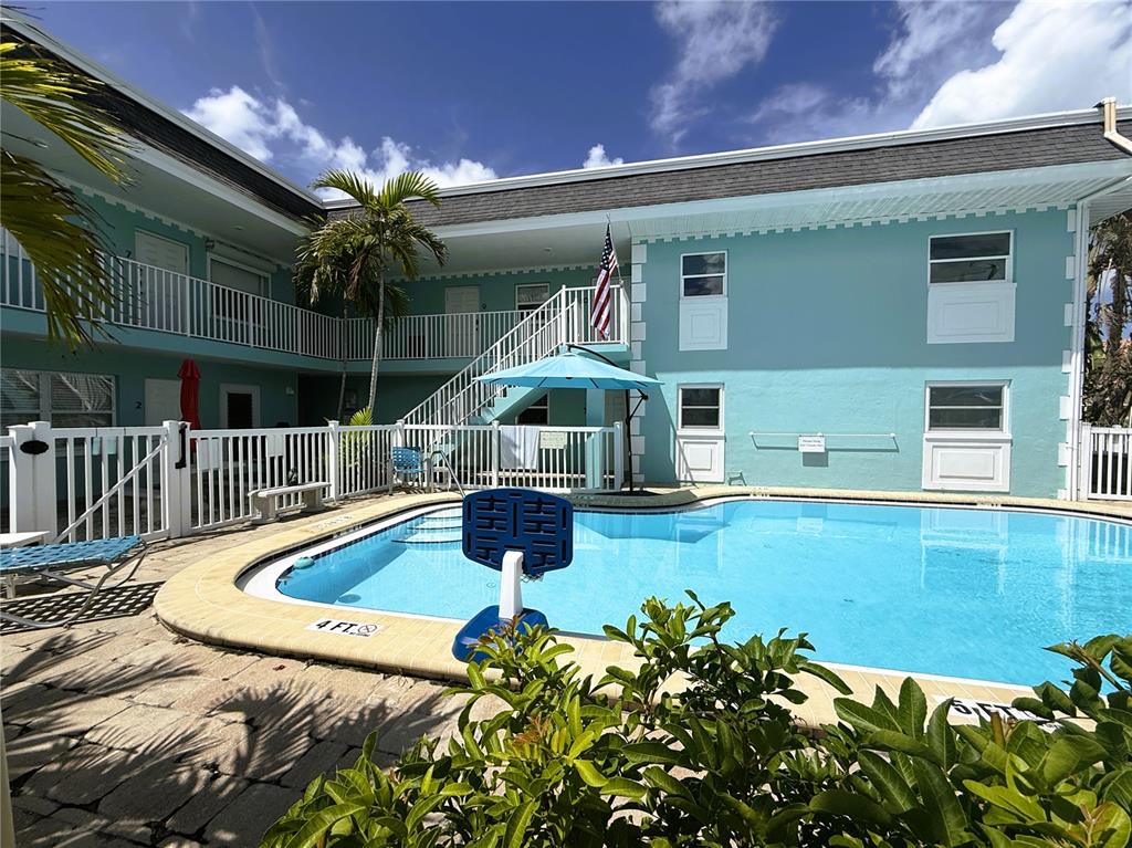 A swimming pool sits in the courtyard of a two-story teal apartment building — 11440 1ST STREET E UNIT 2, TREASURE ISLAND, FL