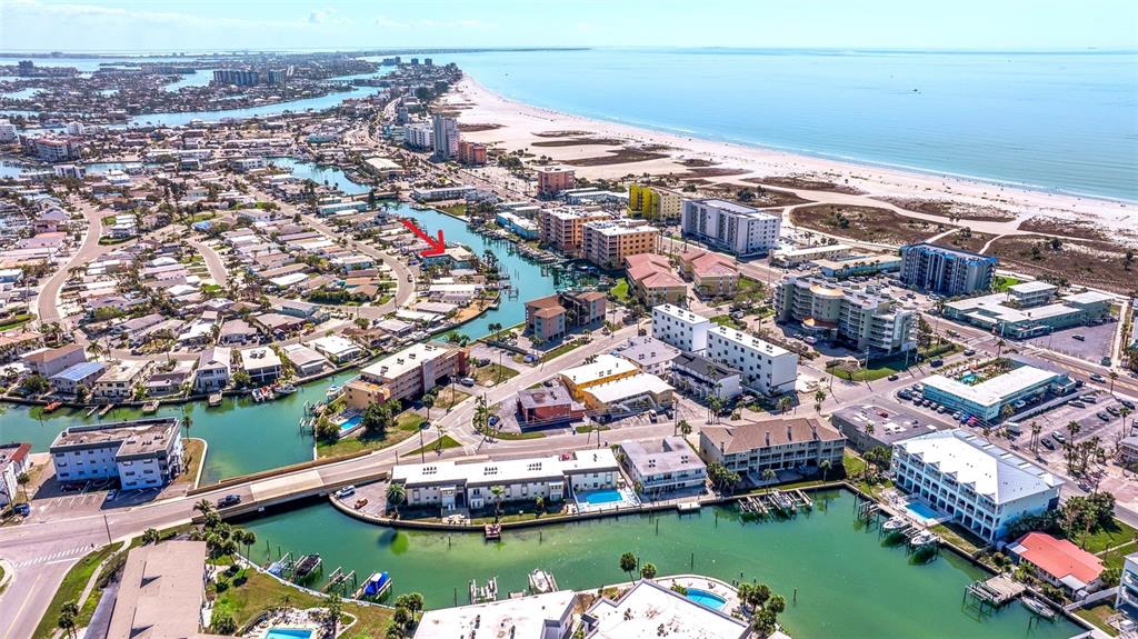 An aerial view shows a coastal town with buildings, canals, and a sandy beach — 11440 1ST STREET E UNIT 2, TREASURE ISLAND, FL