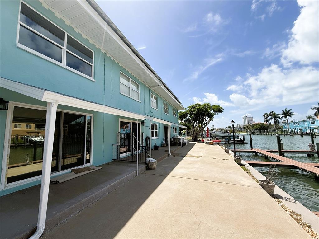 A light blue two-story building features a concrete patio overlooking a canal with boat docks — 11440 1ST STREET E UNIT 2, TREASURE ISLAND, FL