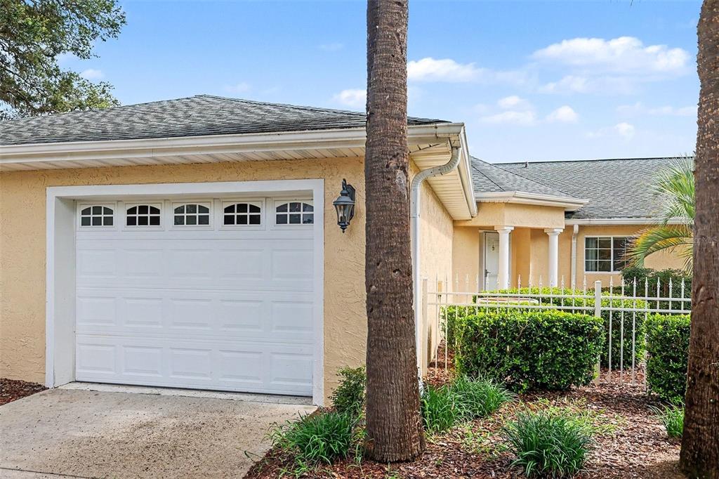 A single-story house exterior featuring a white garage door, tan stucco walls, and landscaping — 13646 SW 115TH AVENUE, DUNNELLON, FL