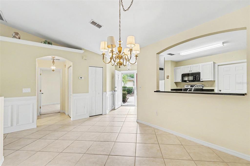 A dining area with tile floors, a chandelier, and a pass-through window to the kitchen — 13646 SW 115TH AVENUE, DUNNELLON, FL