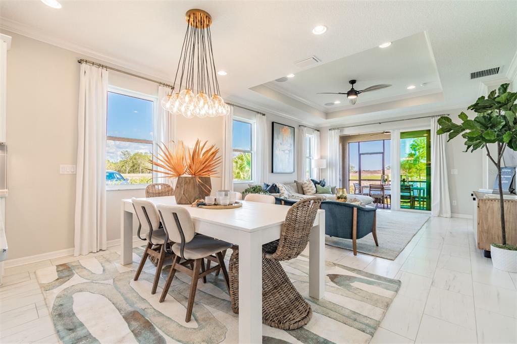 A bright dining area with a white table and modern chandelier opens into a living room — 1649 ROYAL COURT, PORT CHARLOTTE, FL
