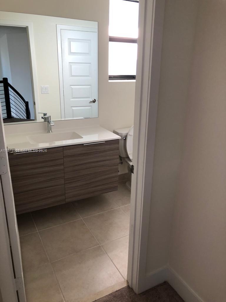 A bathroom features a floating wood-grain vanity, a white countertop, and a wall-mounted mirror — 16045 NW 87th Ct, Miami Lakes FL 33018, MIAMI LAKES, FL