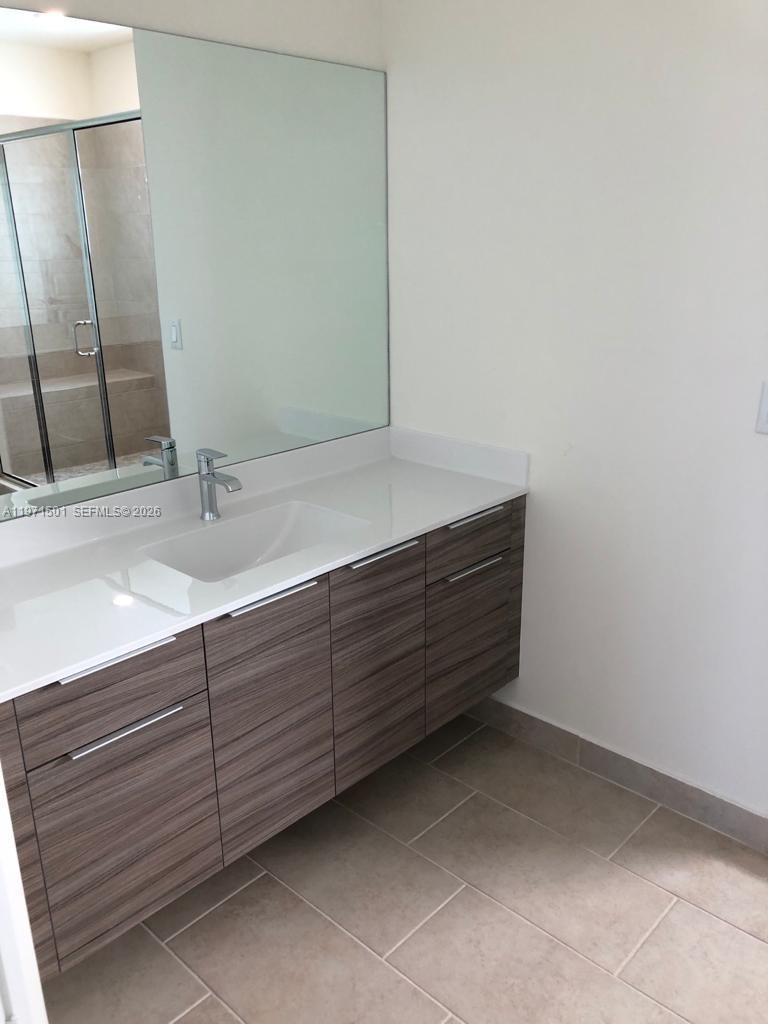 A modern bathroom features a floating wood-grain vanity with a white countertop and large mirror — 16045 NW 87th Ct, Miami Lakes FL 33018, MIAMI LAKES, FL
